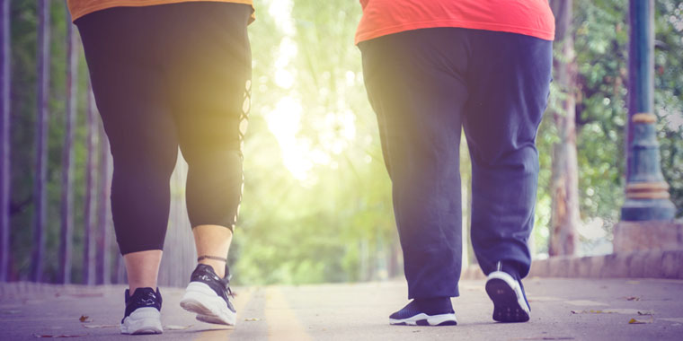 Two overweight people walk outside in the early morning